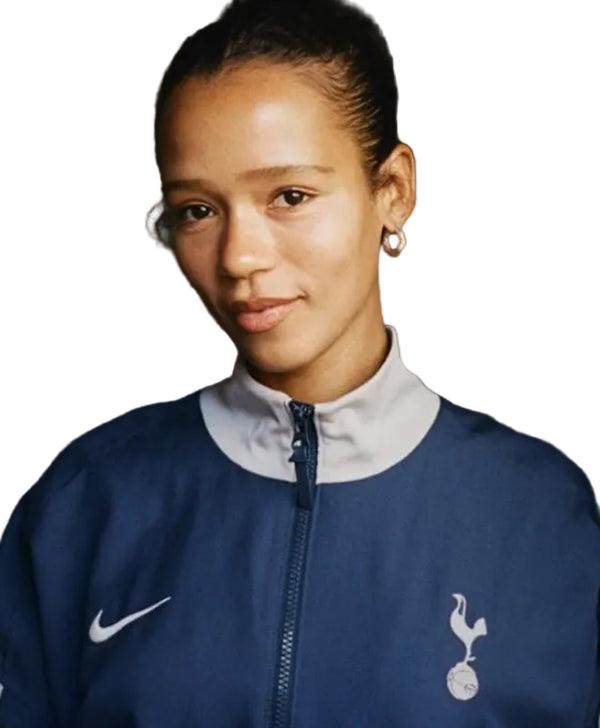 A woman wearing a navy blue Nike Tottenham Hotspur track jacket with a white collar, featuring the white Nike swoosh and the Tottenham Hotspur cocker logo.