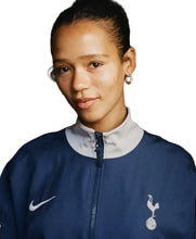 A woman wearing a navy blue Nike Tottenham Hotspur track jacket with a white collar, featuring the white Nike swoosh and the Tottenham Hotspur cocker logo.