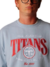 A close-up of a person wearing a light blue crewneck sweatshirt with a red and white graphic that reads 'TITANS NASHVILLE, TN Est. 1960' and 'Have It Nice Game'.