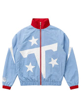 A light blue windbreaker jacket featuring a bold white graphic on the front with three white stars and a large white letter 'T', accented by a red collar, red zipper, and red cuffs.