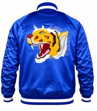 A royal blue satin bomber jacket shown from the back, featuring a large embroidered roaring tiger face graphic in yellow, orange, black, white, and red across the center.