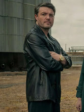 Man wearing a dark jacket standing outdoors with a cloudy sky.