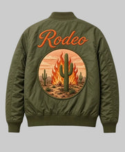 An olive green bomber jacket shown from the back, featuring a large circular desert graphic with a cactus on fire and the word 'Rodeo' embroidered in orange above it.