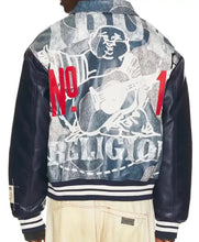 Back view of a varsity-style jacket with navy leather sleeves and a distressed blue denim back panel featuring a large white graphic illustration, red 'NO. 1' text, and 'RELIGION' lettering, worn over light beige pants.