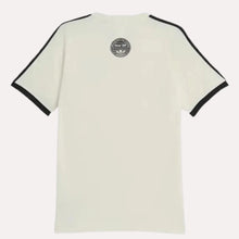 A short-sleeve ringer t-shirt shown from the back, featuring a warm off-white body with black contrast trim on the sleeve cuffs and shoulders, and a circular black graphic printed at the upper center back.
