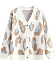 A women's knit cardigan sweater with a white base and an abstract leopard print pattern in tan, light blue, and beige, featuring a V-neck, button-up front, and ribbed trim.