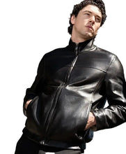 A man wearing a black leather jacket with a high collar and front zipper, standing outdoors in front of modern glass buildings.