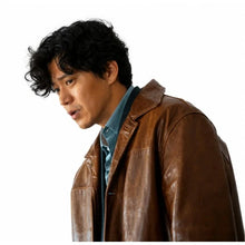 A man wearing a brown leather jacket over a blue collared shirt, shown in a side-profile portrait against a plain white background.