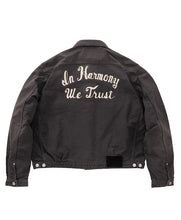 A dark gray washed denim jacket shown from the back, featuring the phrase 'In Harmony We Trust' embroidered in white script across the upper back.