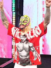 A person wearing a red graphic T-shirt with a large black-and-white wrestler print and white 'WWE' lettering, paired with a yellow lucha mask, standing with arms raised on a stage-like background.