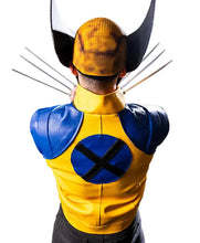 A person shown from behind wearing a yellow and blue Wolverine-style costume with metallic-looking claws extended, photographed in a studio setting with a black backdrop.