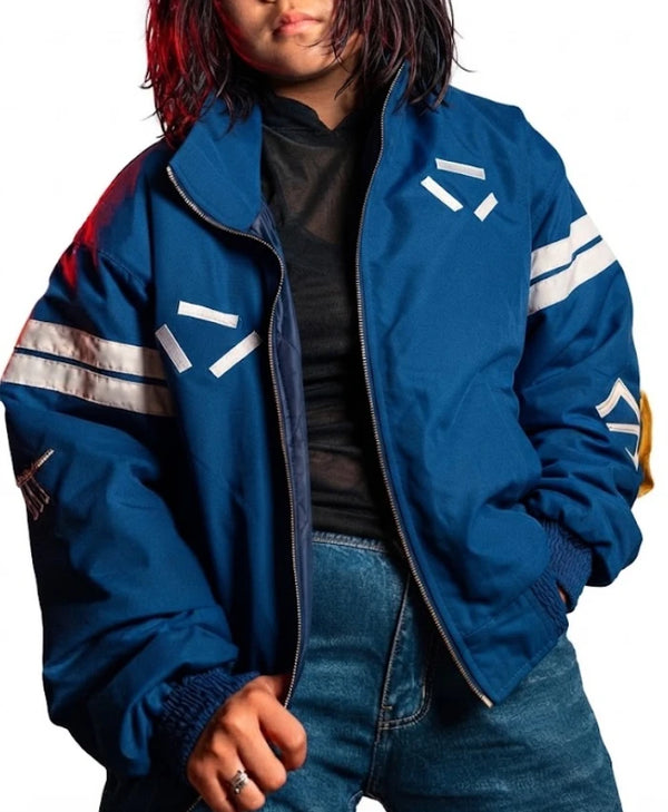 A person wearing a blue oversized zip-up jacket with white geometric stripe graphics on the chest and sleeves, layered over a black top and blue jeans, against a plain white background.